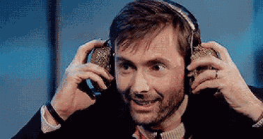 a man wearing headphones is smiling and holding a microphone to his ear .