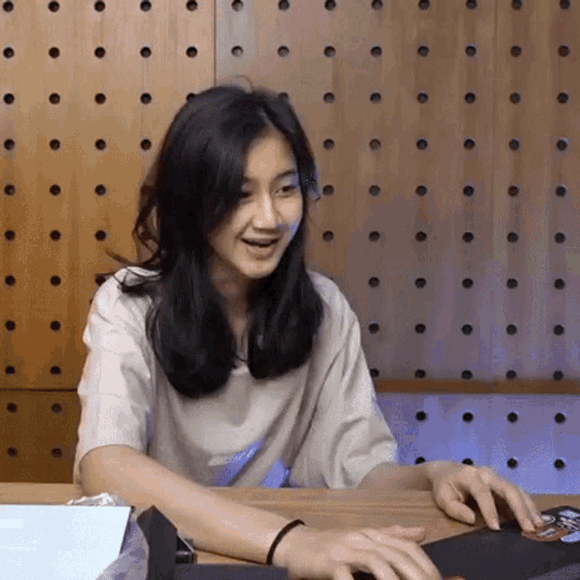 a young woman is sitting at a table with her hands on a mouse pad and smiling .