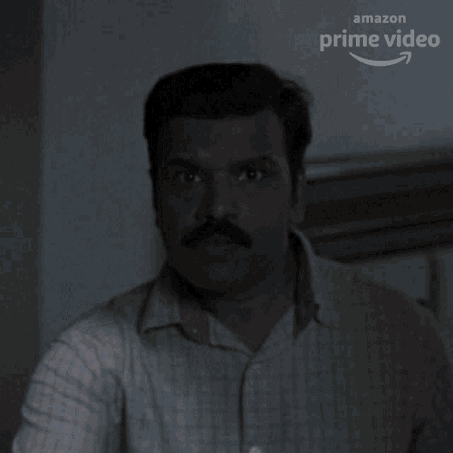 a man with a mustache is looking at the camera with an amazon prime video logo in the background