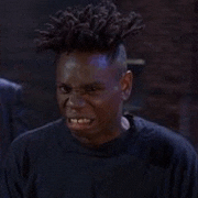 a man with dreadlocks on his head is making a funny face in a dark room .