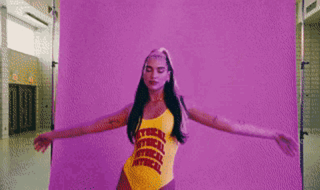 a woman in a yellow one piece swimsuit is dancing in front of a purple background .