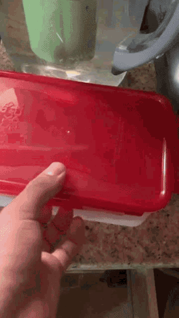 a person is opening a red plastic container on a countertop