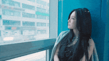a woman stands in front of a window with a blue wall
