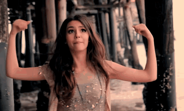 a woman flexes her muscles in front of a wooden structure