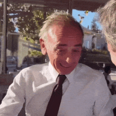 a man in a white shirt and tie is smiling and talking to another man