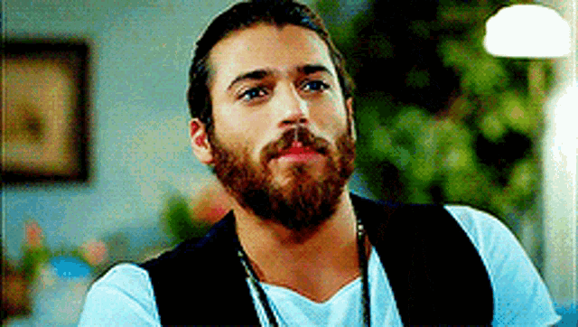 a man with a beard and mustache is wearing a vest and a necklace .