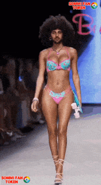 a woman in a bikini walks down a runway with sommi fan token on the bottom right