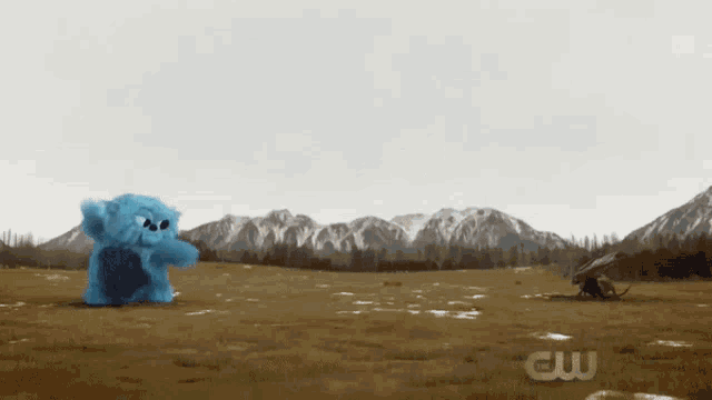 a blue stuffed animal is standing in a field with the letters cw visible