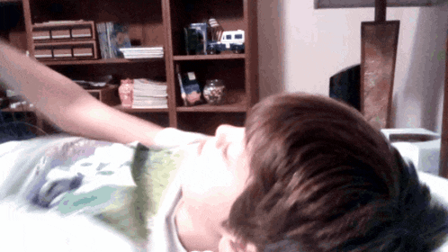 a boy laying on a bed with his arm outstretched in front of a bookshelf