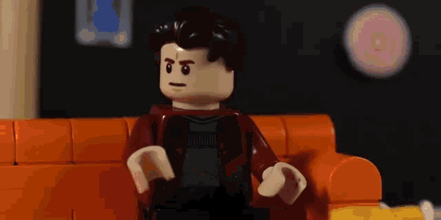a lego man is sitting on an orange couch and looking at something .