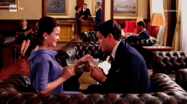 a man and a woman are sitting on a leather couch and drinking wine from a glass