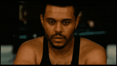 a man with a beard and a black tank top looks at the camera