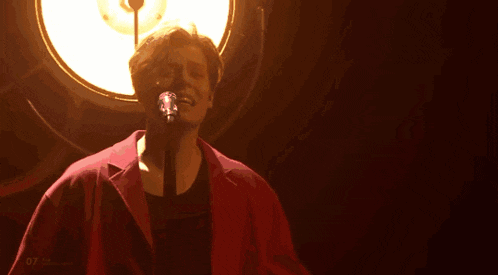 a man in a red shirt is singing into a microphone in a dark room