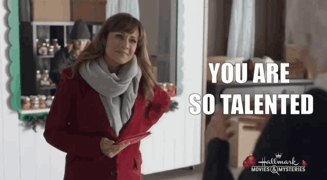 a woman in a red coat and scarf is holding a piece of paper and talking to someone .