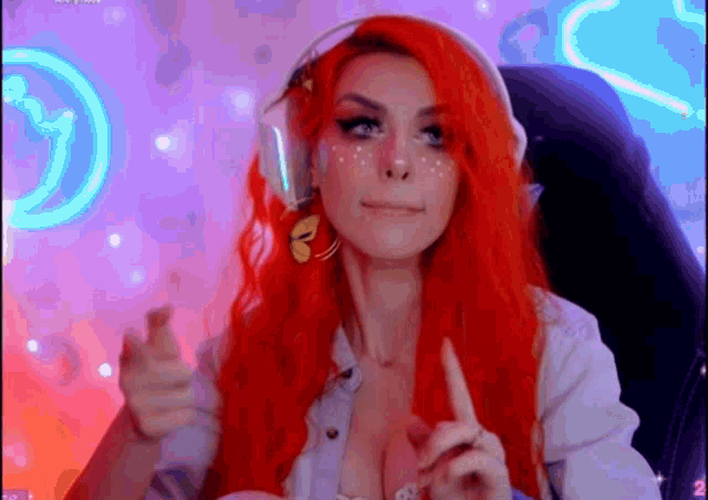a woman with red hair is sitting in a chair wearing headphones and pointing at the camera .