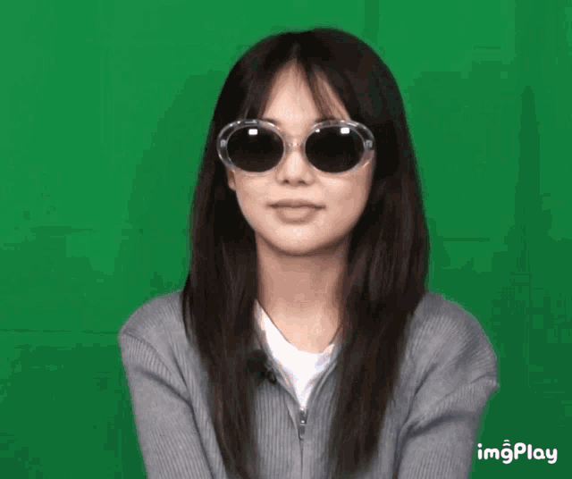 a woman wearing sunglasses and a grey sweater against a green background with imgplay written below her