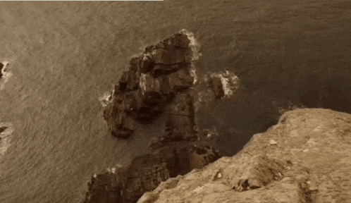 a cliff overlooking a body of water with rocks in the water