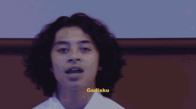 a young man with curly hair is wearing a white shirt with the word gadisku on the bottom right