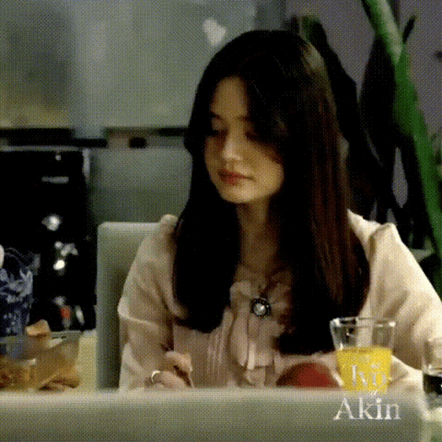 a woman is sitting at a table with a laptop and a glass of orange juice with the name akin on it