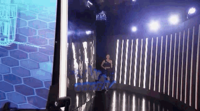 a woman in a black dress is walking through a dark room with a fence .