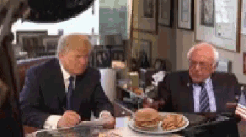 donald trump and bernie sanders are sitting at a table with a plate of food .
