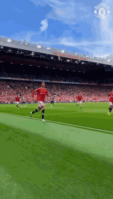 a man in a red shirt is running on a soccer field in front of a manchester united stadium