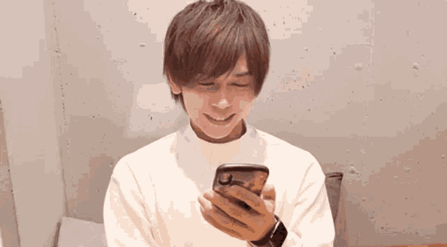 a young man is smiling while holding a cell phone in his hand .