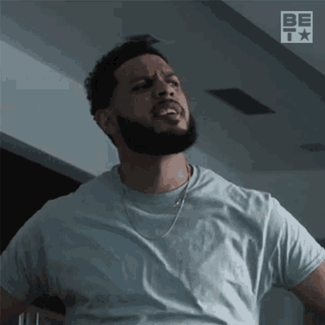 a man with a beard is wearing a light blue t-shirt and a gold chain around his neck