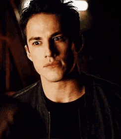 a man wearing a black jacket and a black shirt is looking at the camera in a dark room .