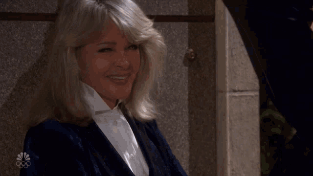 a woman in a tuxedo is smiling in front of a wall with the nbc logo on it