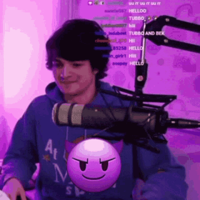 a man in a blue hoodie is standing in front of a microphone with a purple smiley face hanging from it .