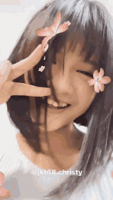 a girl with a flower in her hair is smiling and giving a peace sign