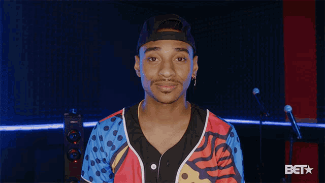 a man in a colorful shirt is standing in front of a microphone with the word bet on the bottom
