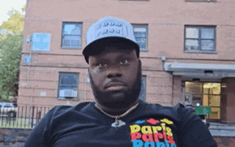 a man wearing a hat and a shirt that says paris park park is sitting in front of a building .