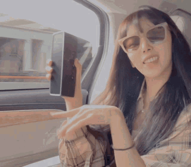 a woman wearing sunglasses is sitting in a car holding a phone