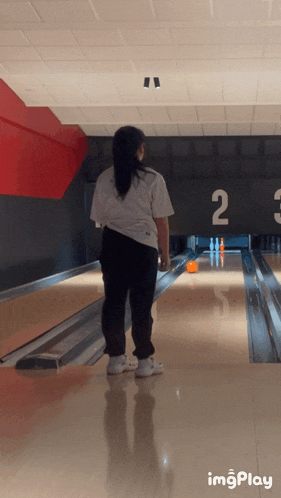 a woman playing bowling in a bowling alley with the number 2 on the wall behind her