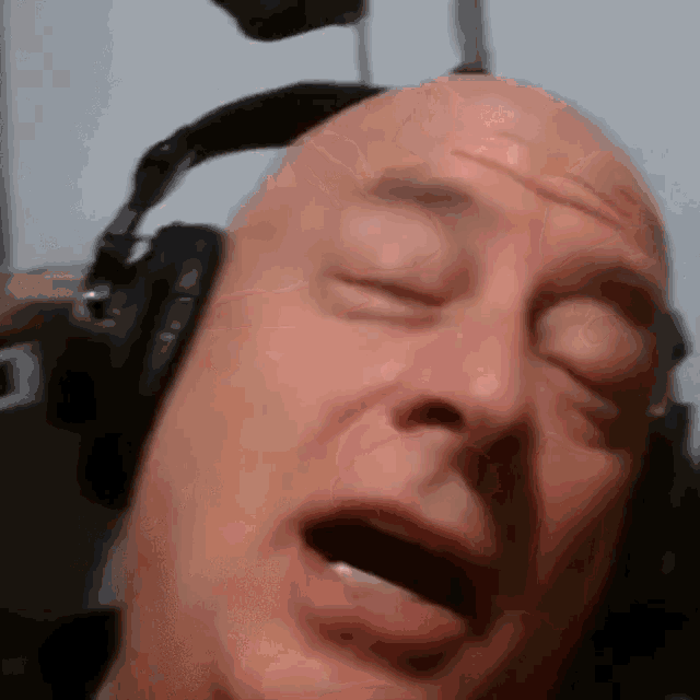 a bald man wearing headphones has his eyes closed
