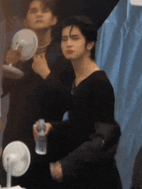 a man in a black dress is holding a bottle of water while looking at himself in a mirror .