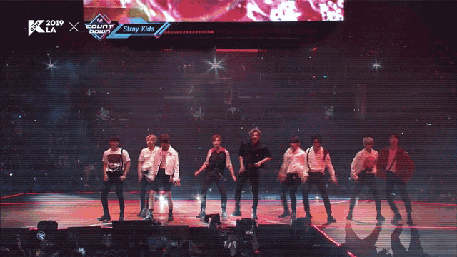 a group of young men are dancing on a stage in front of a screen that says ' stray kids '