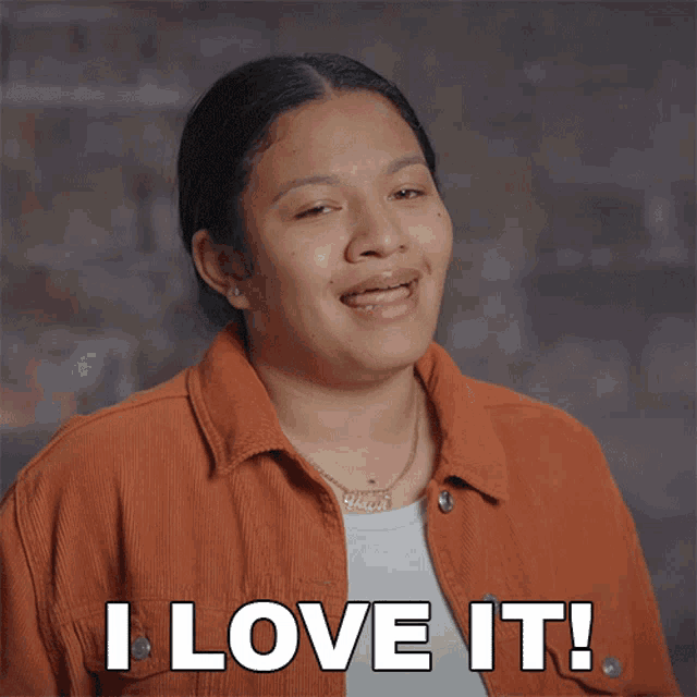 a woman in an orange jacket is smiling and says " i love it "