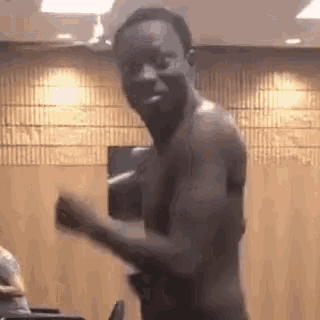 a shirtless man is dancing in a room with a wooden wall .