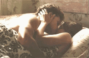 a man and a woman are kissing in bed under a blanket .
