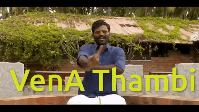 a man in a blue shirt is giving the middle finger in front of a sign that says vena thambi