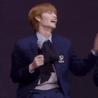 a man in a suit and tie is laughing while holding a microphone in his hand .