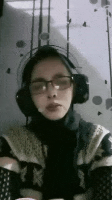 a woman wearing glasses and headphones is talking into a microphone while sitting at a table .
