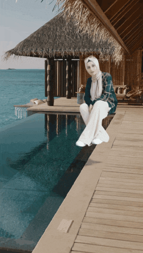 a woman in a hijab sits next to a pool