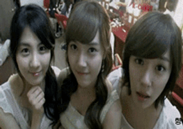 three young women are posing for a picture together and one of them is wearing a white tank top
