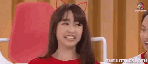 a woman wearing a red shirt and cat ears is making a funny face .