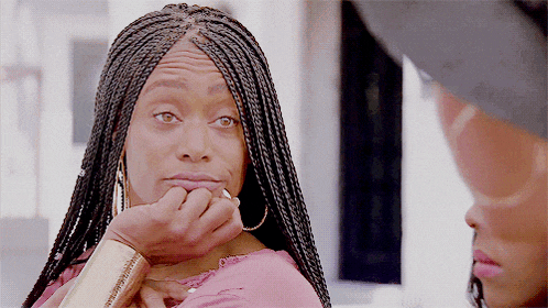 a woman with braids and hoop earrings is making a face with her hand on her chin