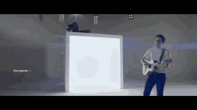 a man is playing a guitar in front of a white cube with the hashtag tuesspezial at the bottom